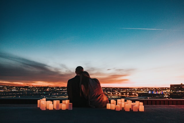 A couple embracing while enjoying the view of a city at sunset.